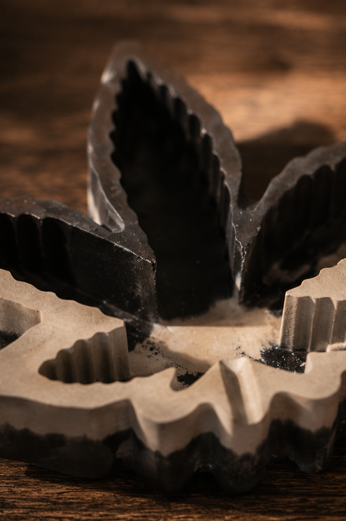 A collage showing a leaf-shaped incense holder and incense sticks in use. The product appears in close-up and in a styled tabletop setting with a hand dipping a incense stick into the holder, on a wooden surface with woven mats and small plants in the background.