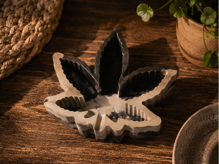 A collage showing a leaf-shaped incense holder and incense sticks in use. The product appears in close-up and in a styled tabletop setting with a hand dipping a incense stick into the holder, on a wooden surface with woven mats and small plants in the background.