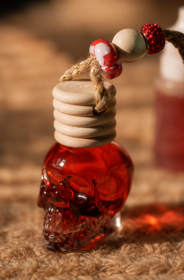 A collage showing a small skull-shaped glass car perfume bottle filled with red liquid, hanging from a rope with decorative beads. The left panel is a close-up of the bottle, while the top-right and bottom-right panels show the bottle in use on a wooden surface and hanging inside a car.